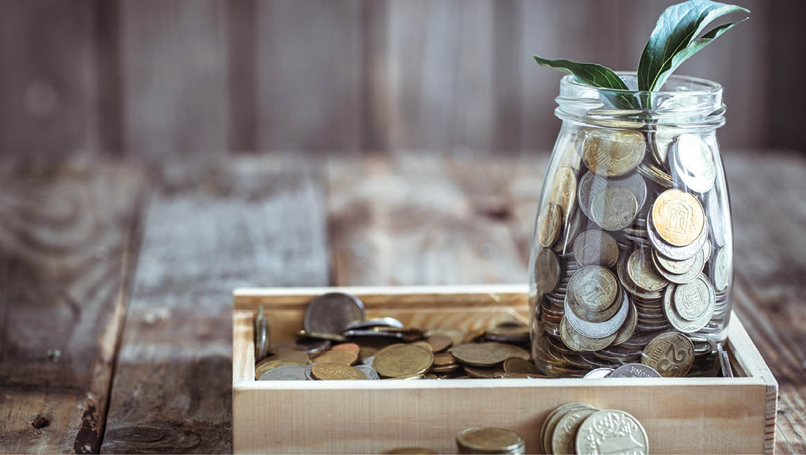 A jar with different coins and green growth growing from above, stand on a wooden background, the concept of growth and saving money